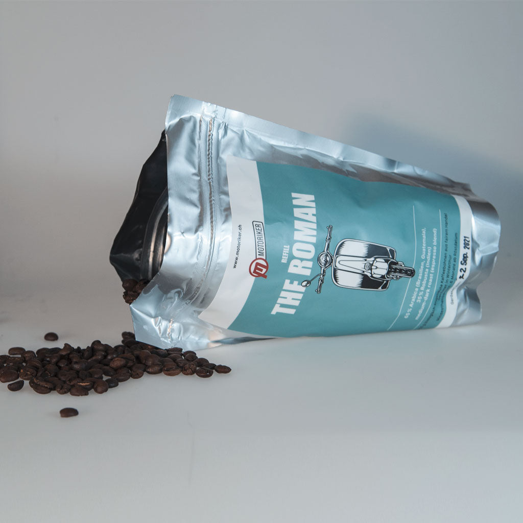 Motoriker Coffee The Roman, liegender silberner Nachfüllbeutel mit blauem Etikett und Kaffeebohnen